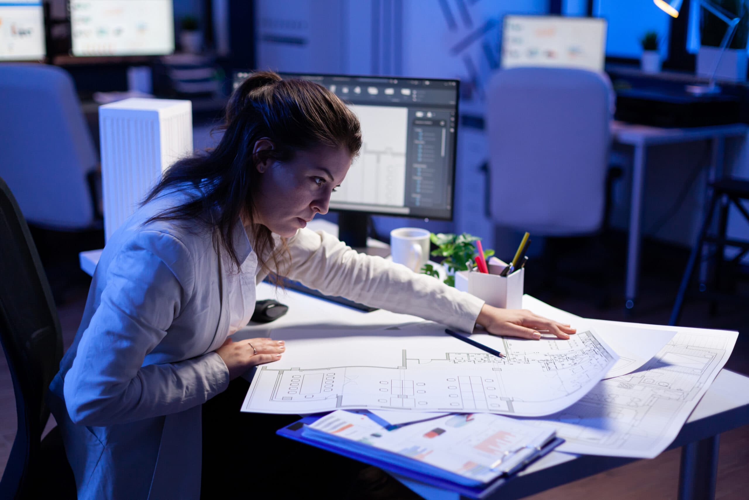 overworked,woman,architect,checking,and,matching,blueprints,sitting,at,office