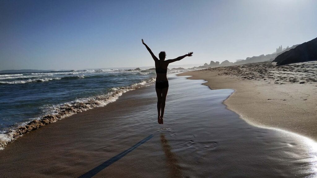 person dancing in freedom along the beach with ocean in view